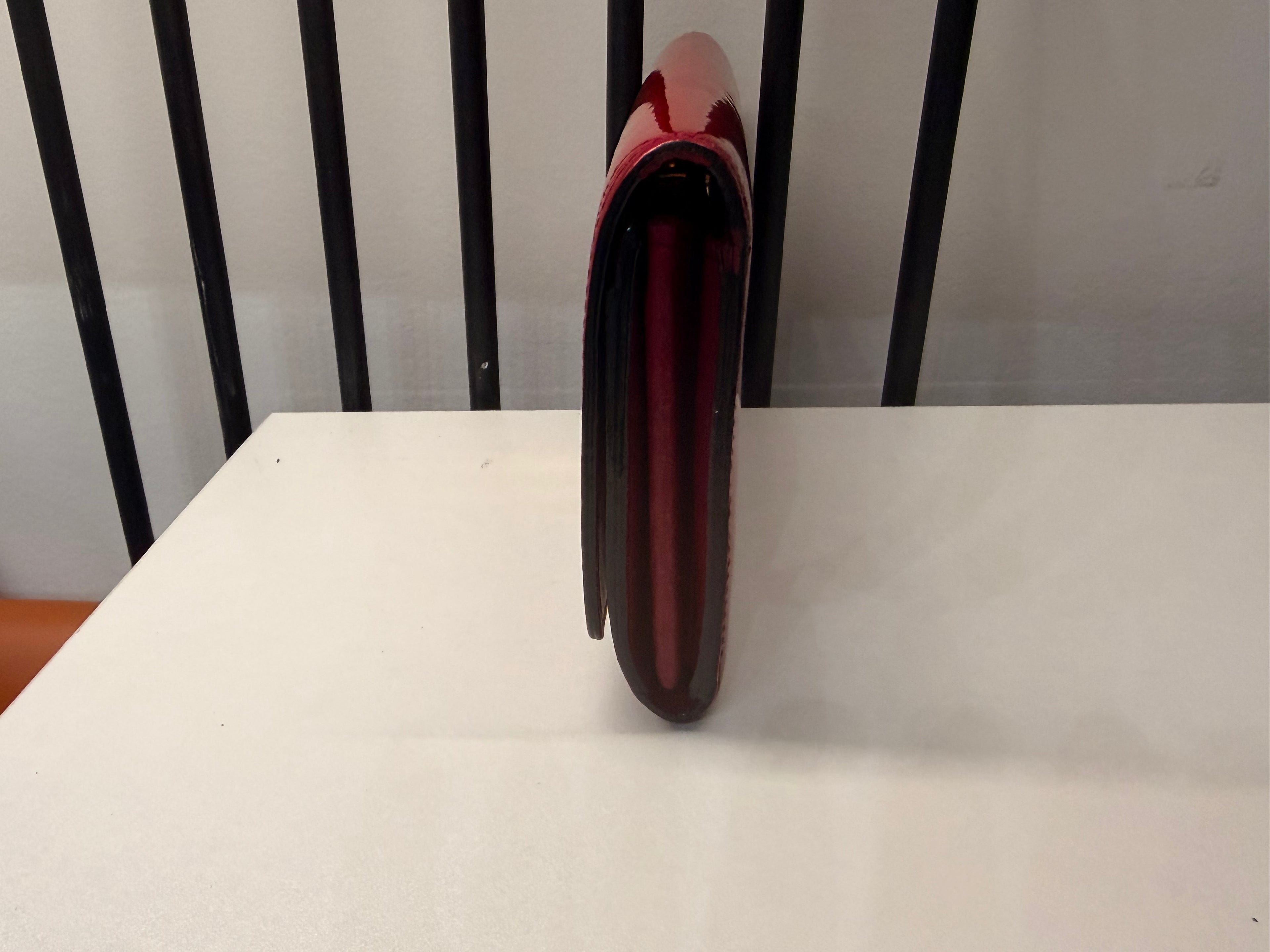 Louis Vuitton long wallet crafted in glossy red patent leather with a large gold-tone LV logo on the front.