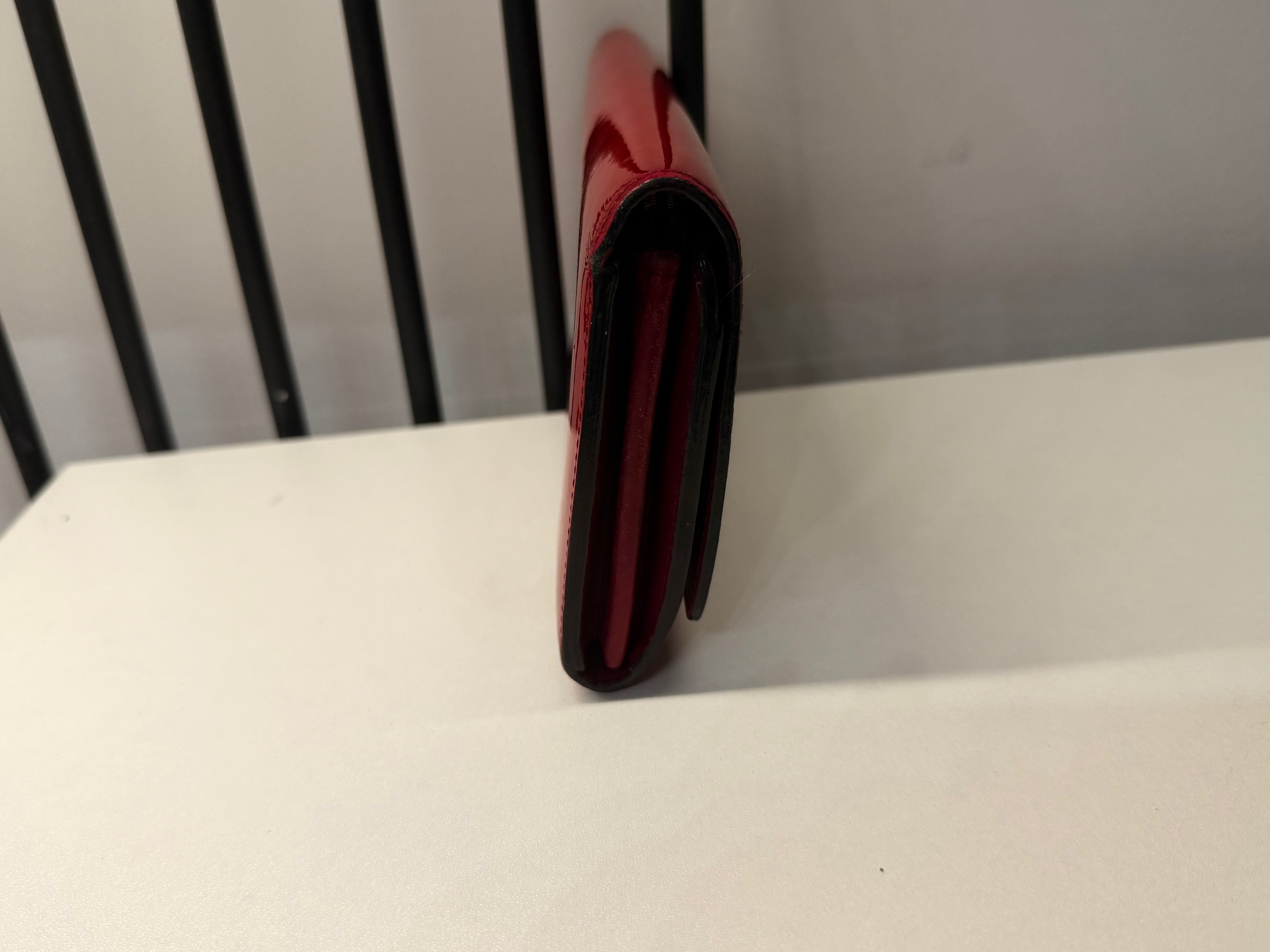 Louis Vuitton long wallet crafted in glossy red patent leather with a large gold-tone LV logo on the front.