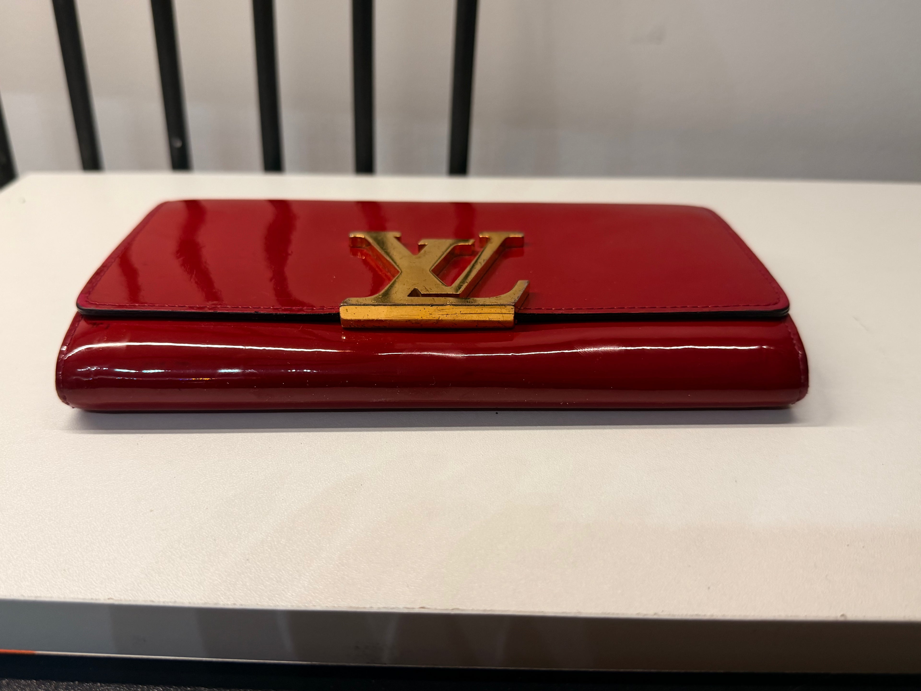 Louis Vuitton long wallet crafted in glossy red patent leather with a large gold-tone LV logo on the front.
