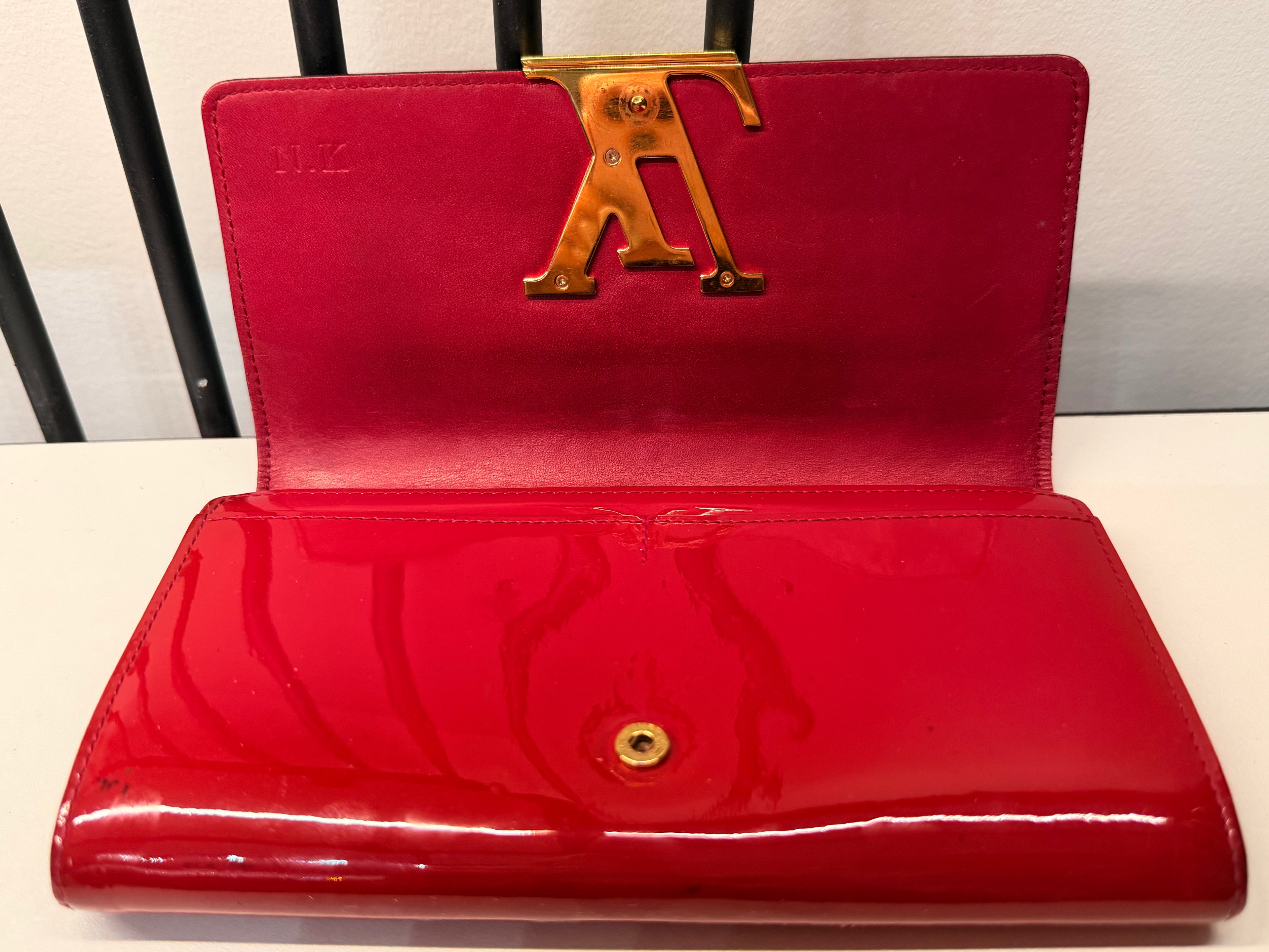 Louis Vuitton long wallet crafted in glossy red patent leather with a large gold-tone LV logo on the front.