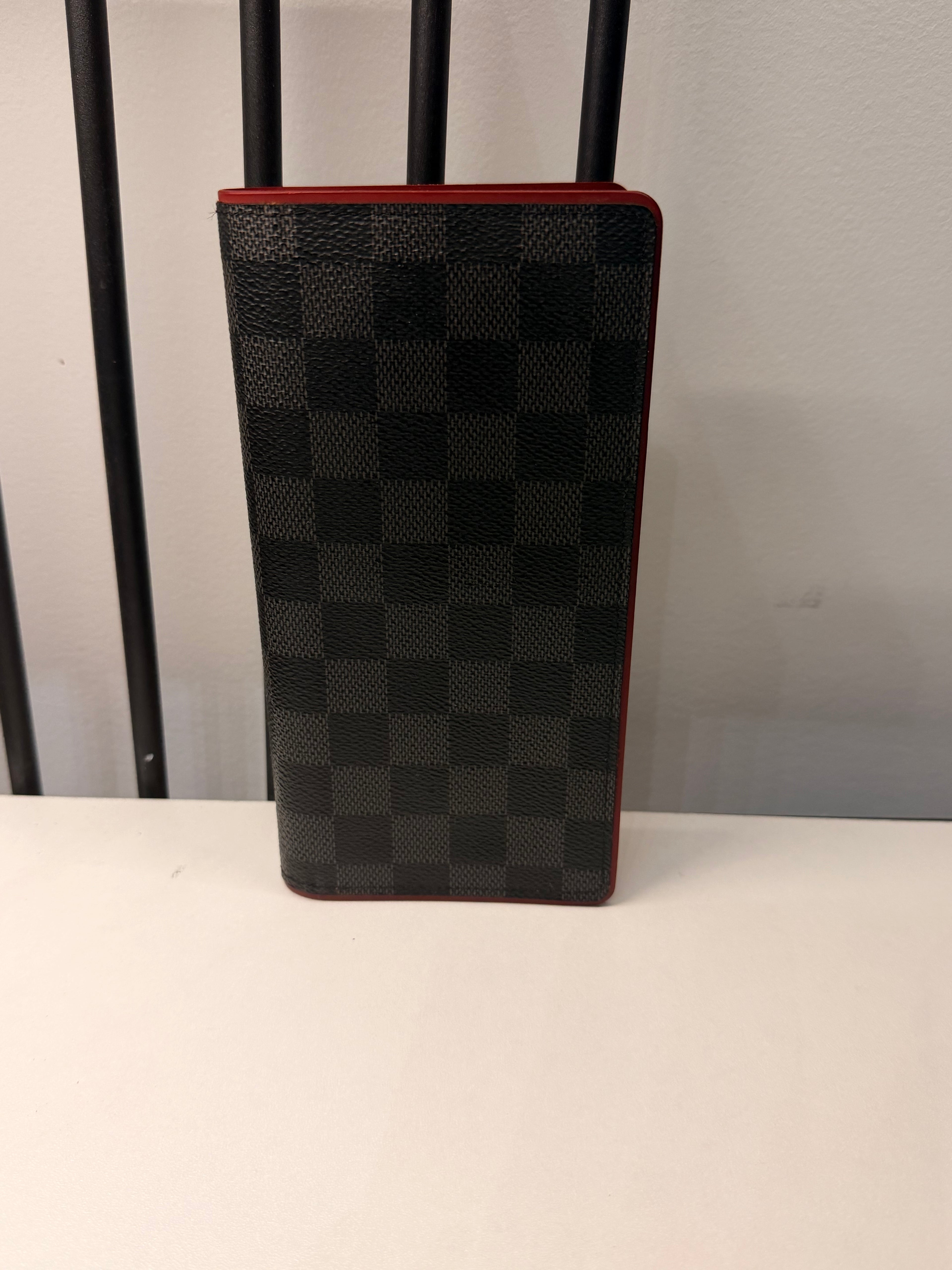 Louis Vuitton long wallet crafted in black and grey Damier Graphite coated canvas with contrasting red leather trim.