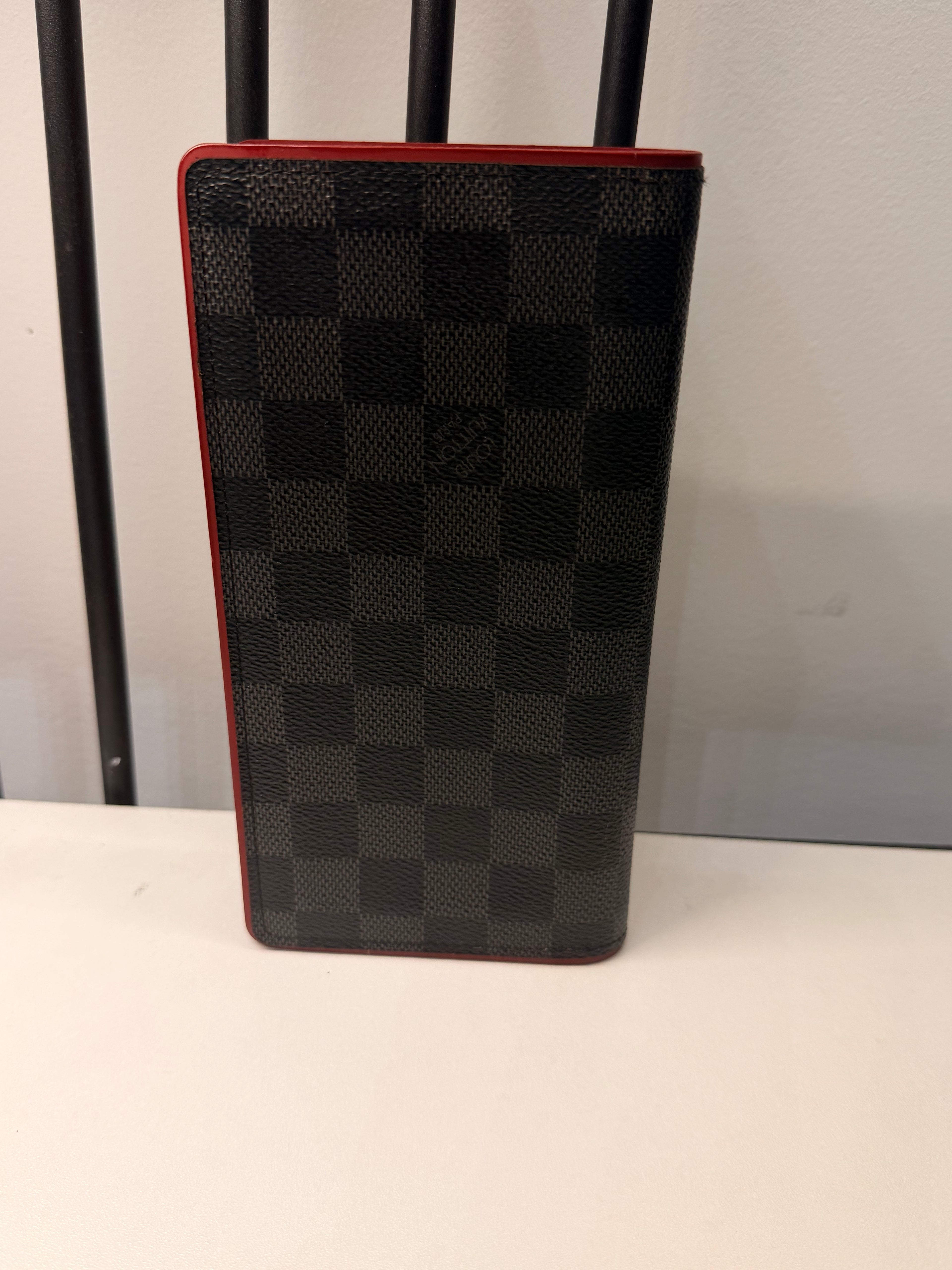 Louis Vuitton long wallet crafted in black and grey Damier Graphite coated canvas with contrasting red leather trim.
