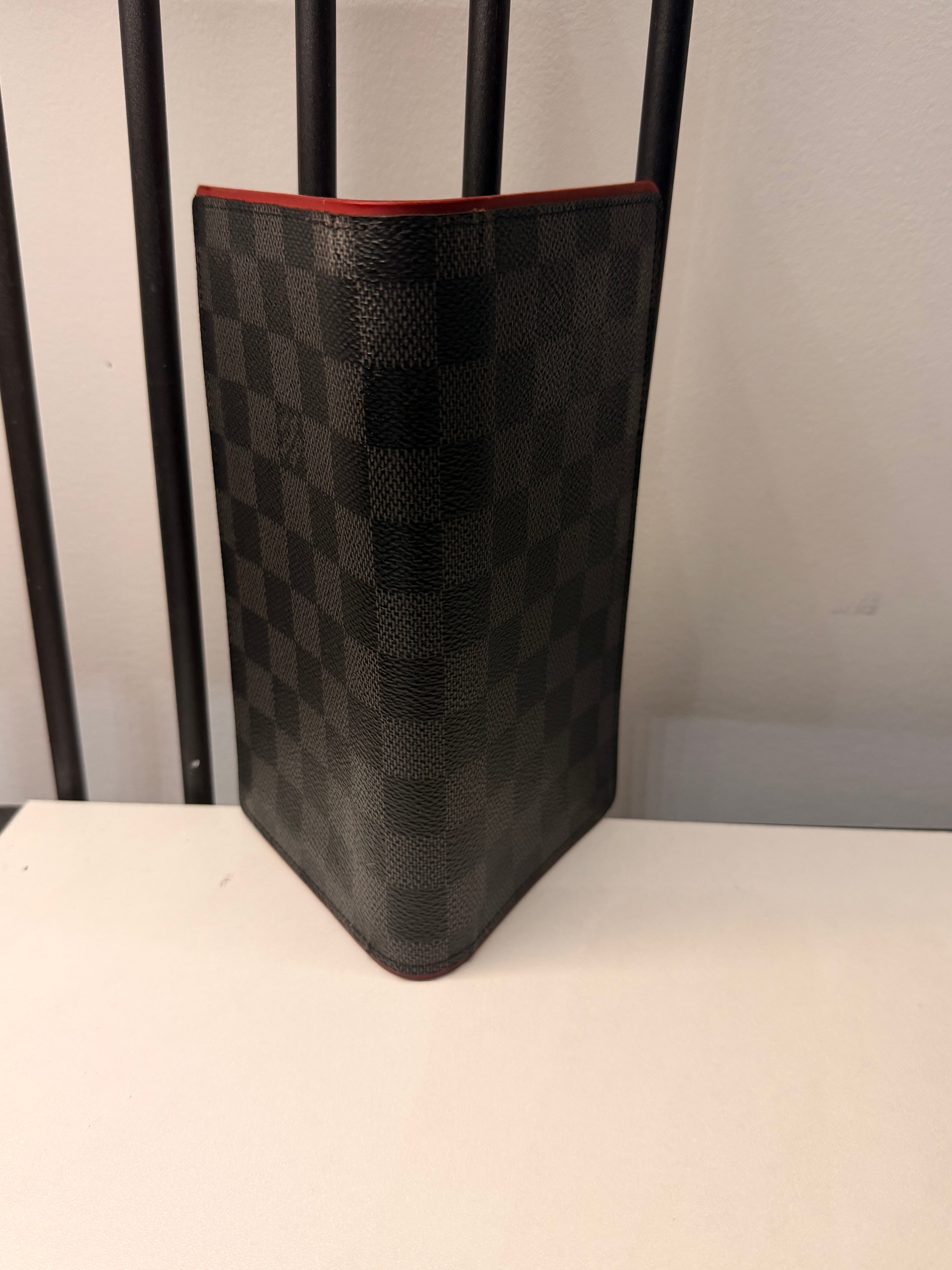 Louis Vuitton long wallet crafted in black and grey Damier Graphite coated canvas with contrasting red leather trim.