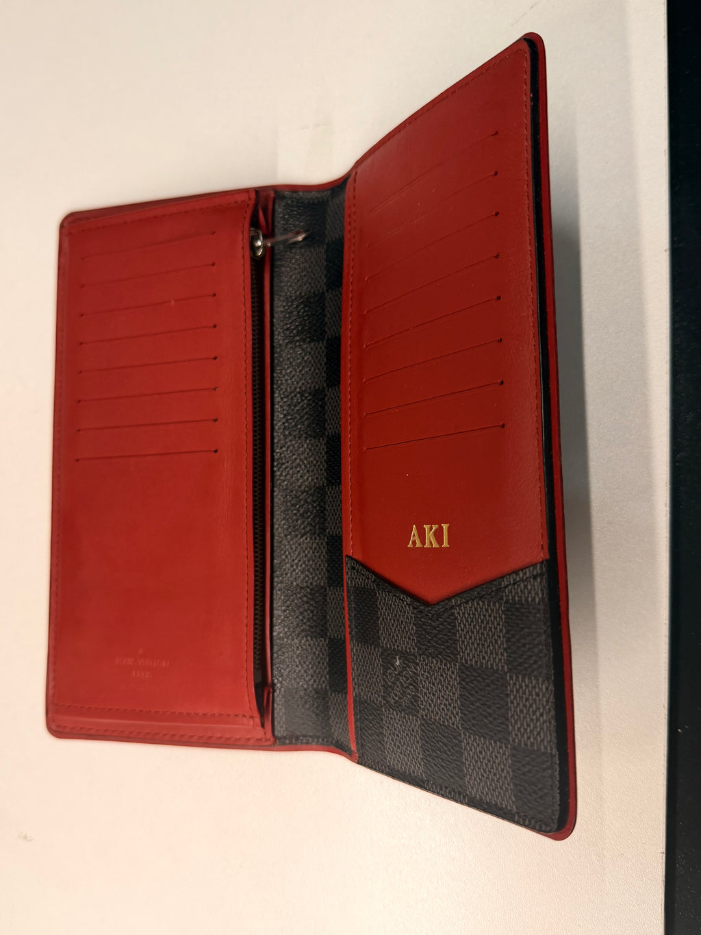 Louis Vuitton long wallet crafted in black and grey Damier Graphite coated canvas with contrasting red leather trim.