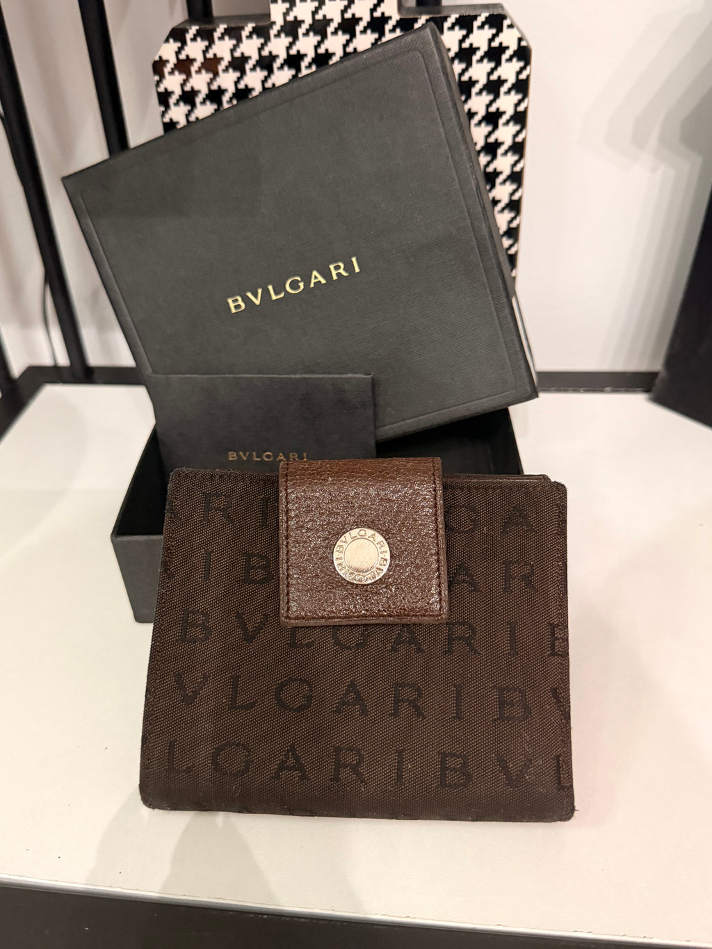 Bvlgari compact wallet featuring the signature Logo Mania monogram fabric in dark brown with matching textured leather trim.