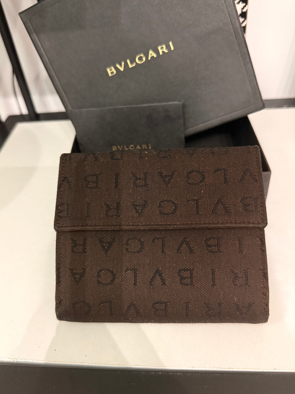 Bvlgari compact wallet featuring the signature Logo Mania monogram fabric in dark brown with matching textured leather trim.