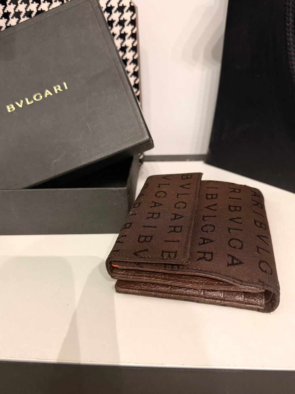 Bvlgari compact wallet featuring the signature Logo Mania monogram fabric in dark brown with matching textured leather trim.