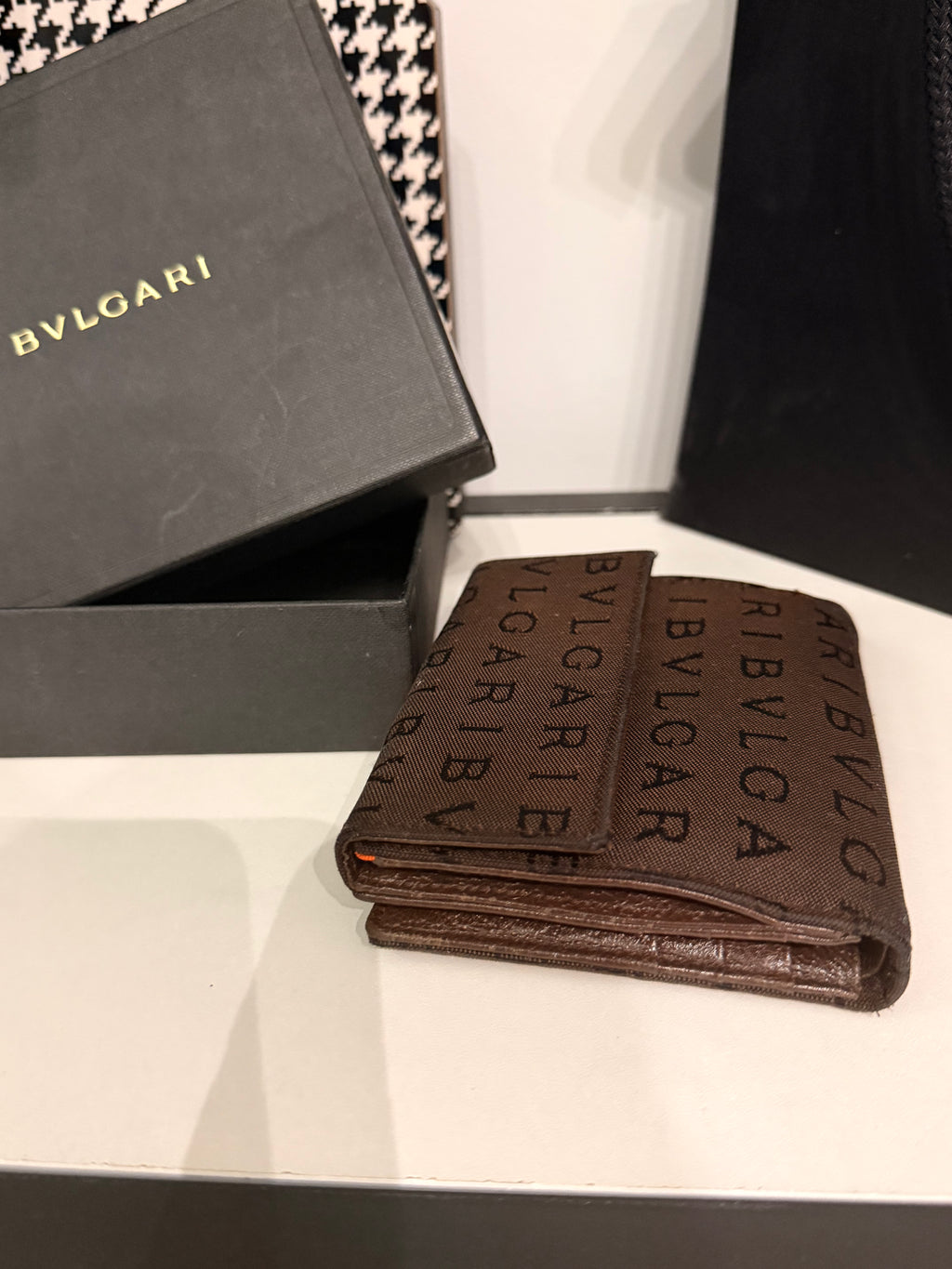 Bvlgari compact wallet featuring the signature Logo Mania monogram fabric in dark brown with matching textured leather trim.