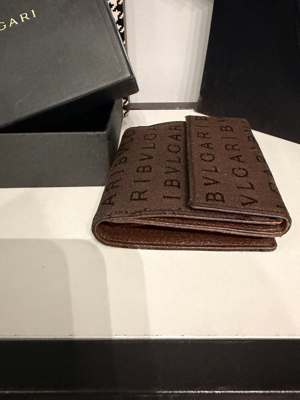 Bvlgari compact wallet featuring the signature Logo Mania monogram fabric in dark brown with matching textured leather trim.