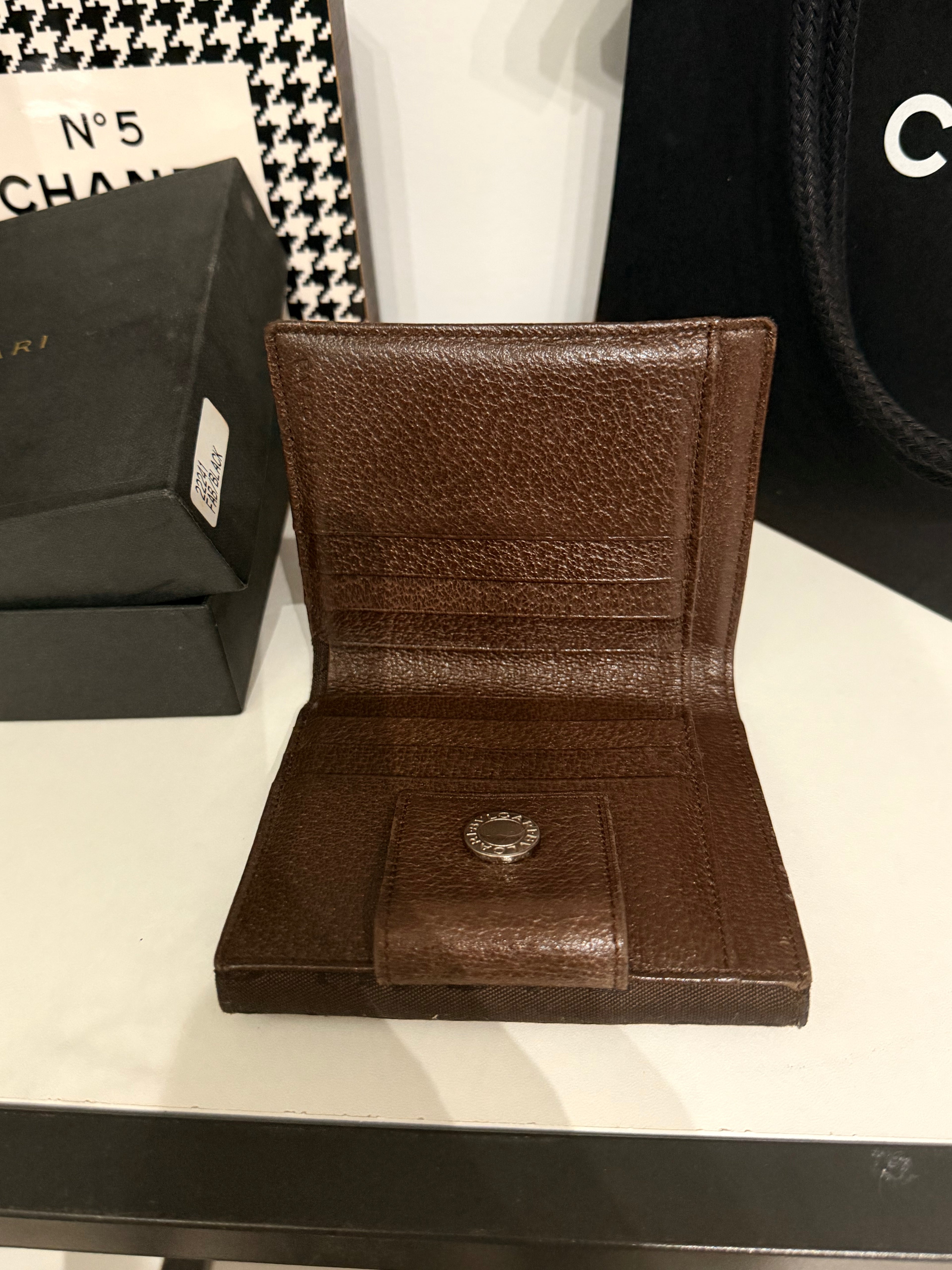 Bvlgari compact wallet featuring the signature Logo Mania monogram fabric in dark brown with matching textured leather trim.