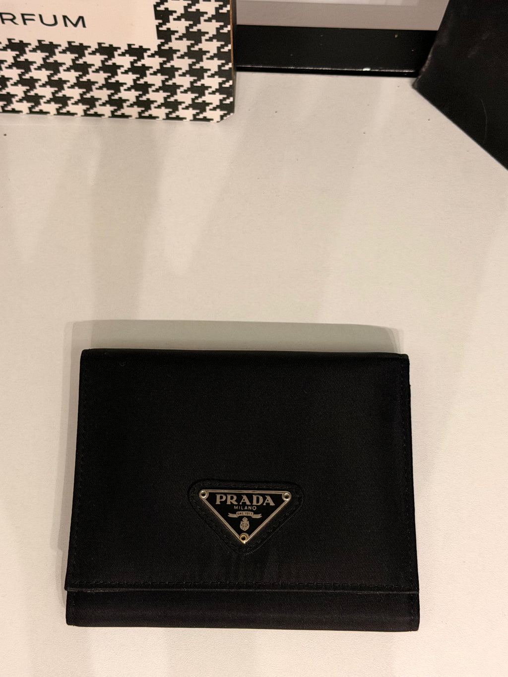 Classic Prada compact wallet crafted from durable black Tessuto nylon and finished with the iconic silver-tone triangular Prada Milano logo plaque.
