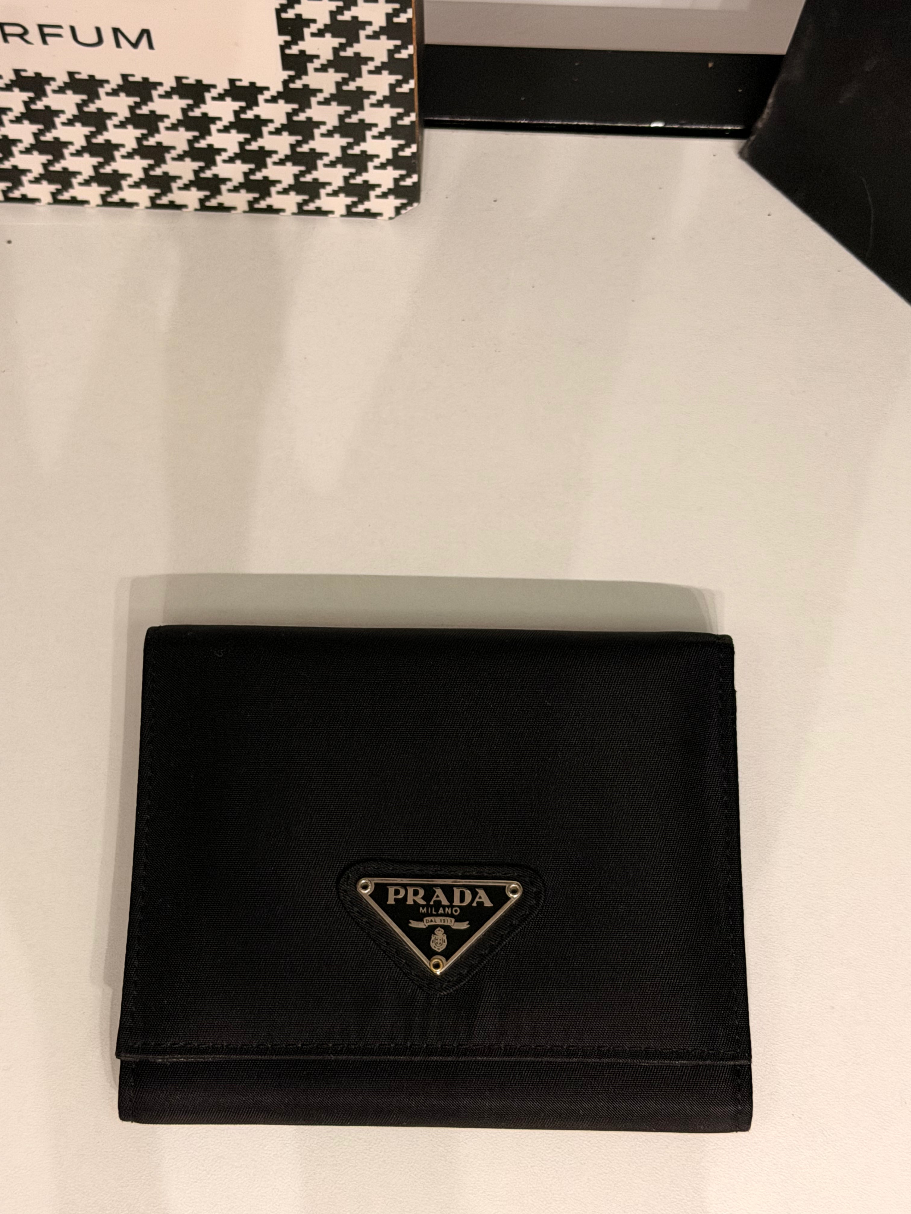 Classic Prada compact wallet crafted from durable black Tessuto nylon and finished with the iconic silver-tone triangular Prada Milano logo plaque.