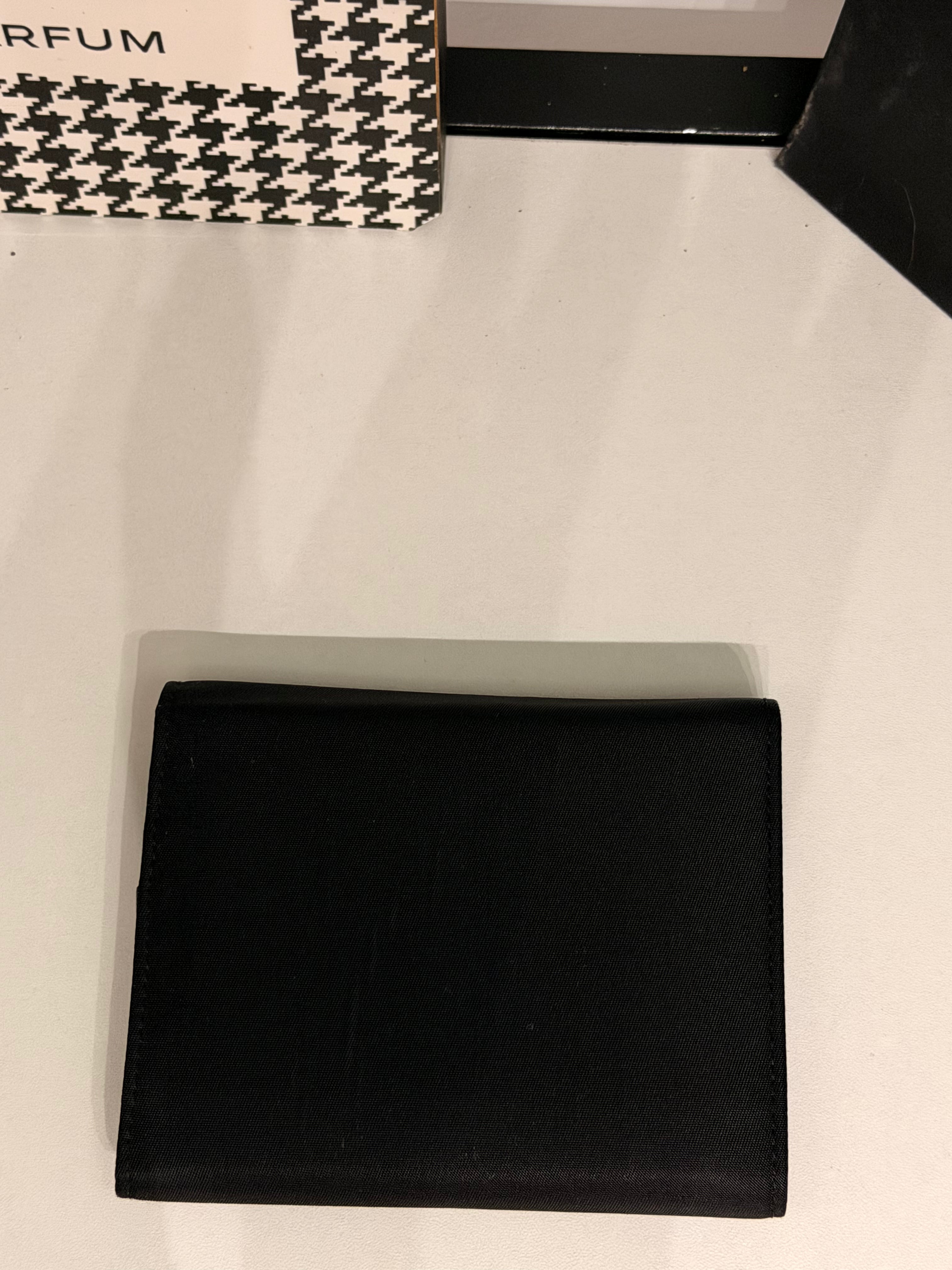 Classic Prada compact wallet crafted from durable black Tessuto nylon and finished with the iconic silver-tone triangular Prada Milano logo plaque.