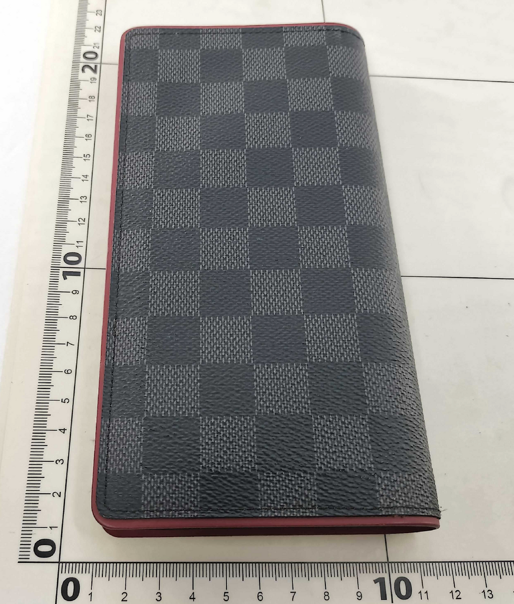 Louis Vuitton long wallet crafted in black and grey Damier Graphite coated canvas with contrasting red leather trim.
