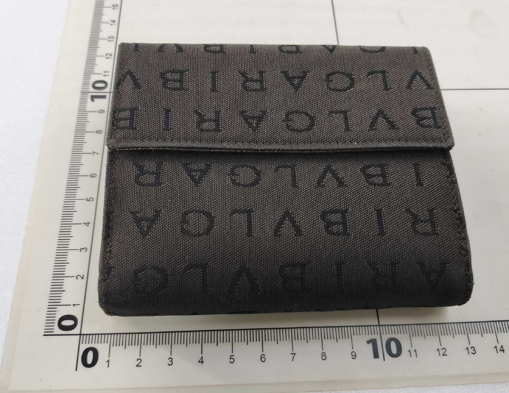 Bvlgari compact wallet featuring the signature Logo Mania monogram fabric in dark brown with matching textured leather trim.