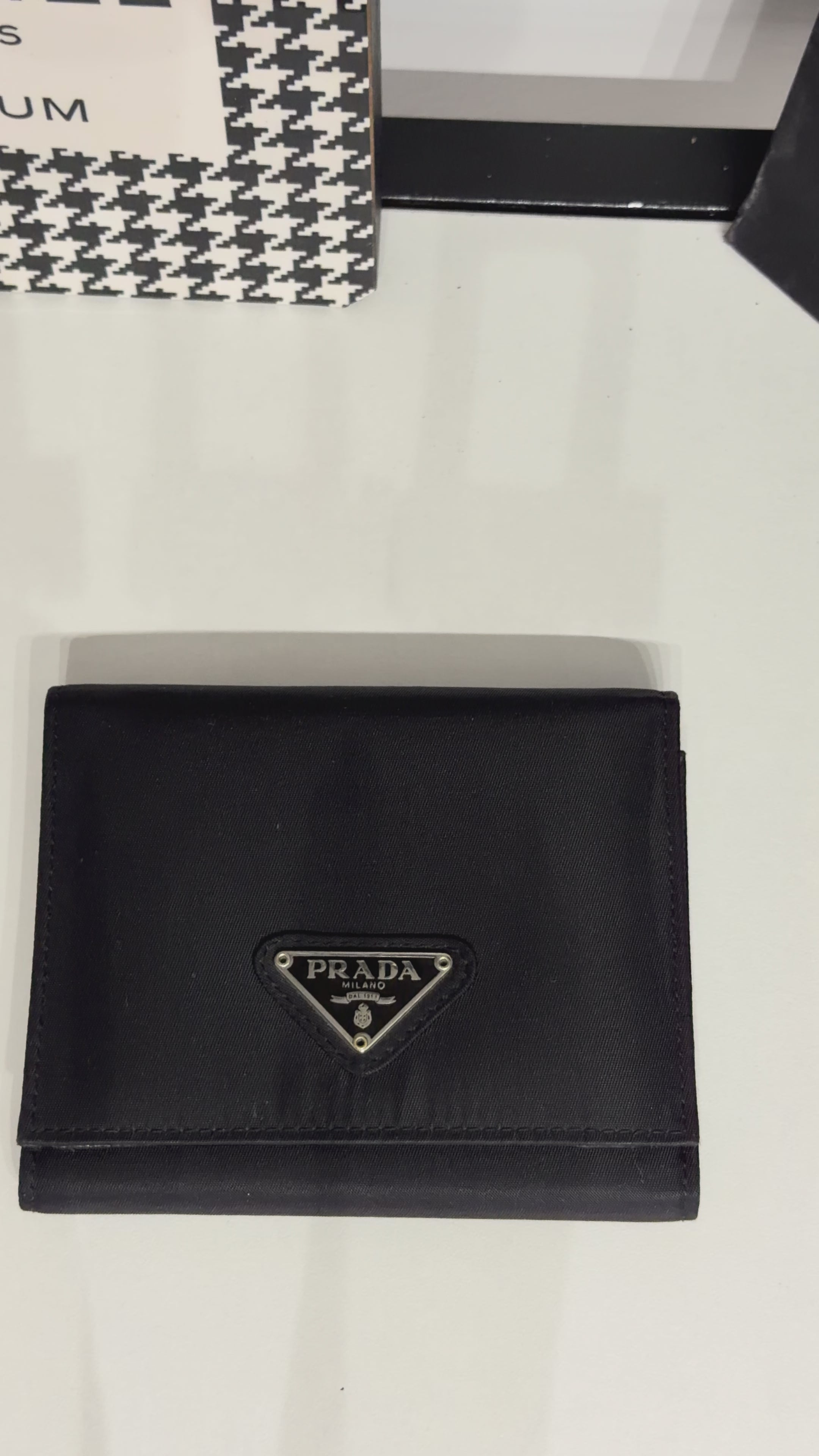 Classic Prada compact wallet crafted from durable black Tessuto nylon and finished with the iconic silver-tone triangular Prada Milano logo plaque.